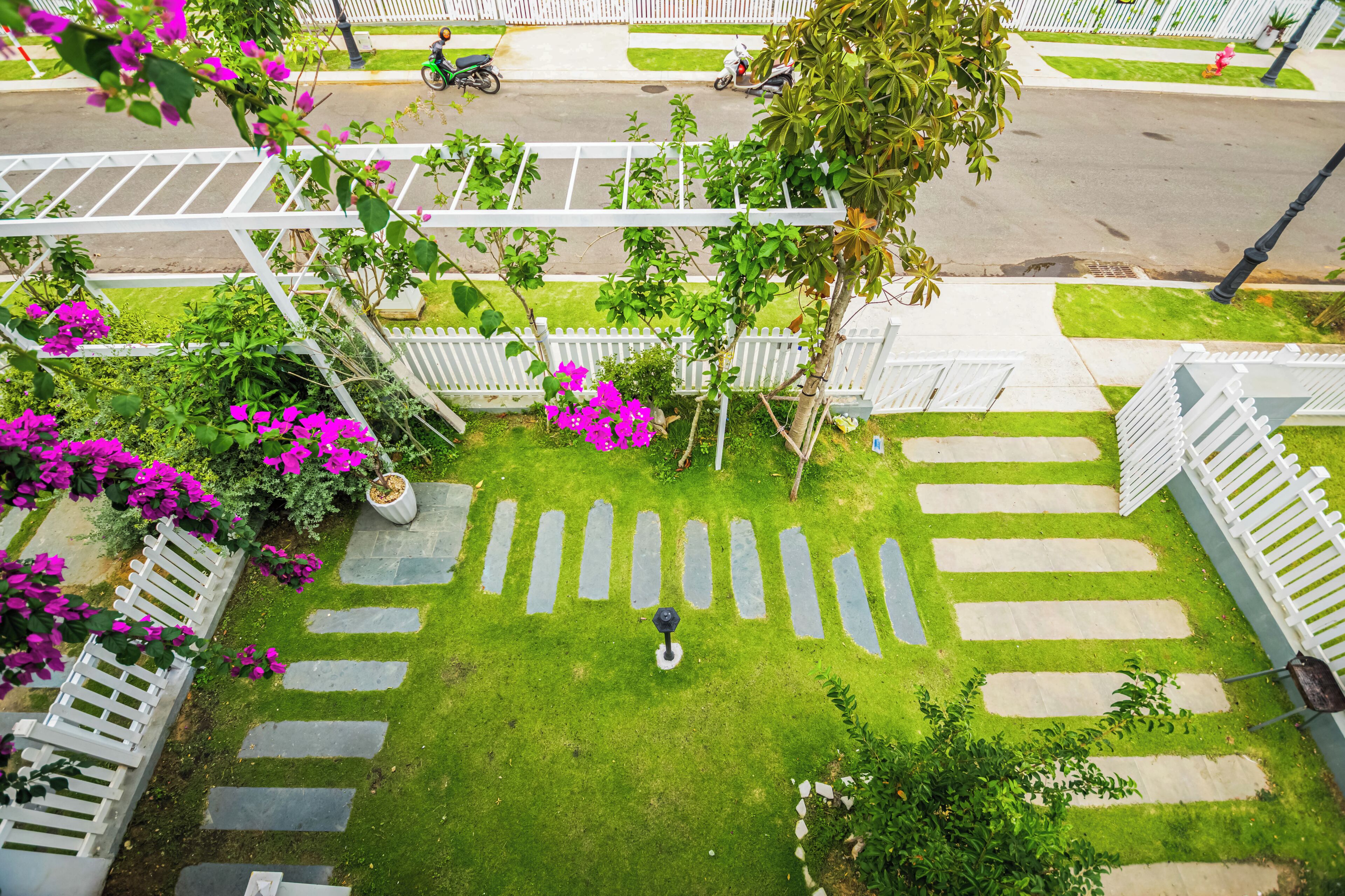 A garden with a white fence, stepping stones, and pink flowers.