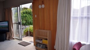 Una habitación con una puerta de vidrio corredera que da a un balcón, una estantería de madera, un televisor y una silla.
