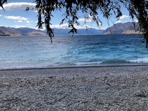Ein Kiesstrand mit Blick auf Berge und einen See.