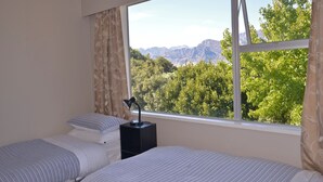 Un dormitorio con dos camas, una mesita de noche y un ventanal con vistas a la montaña.