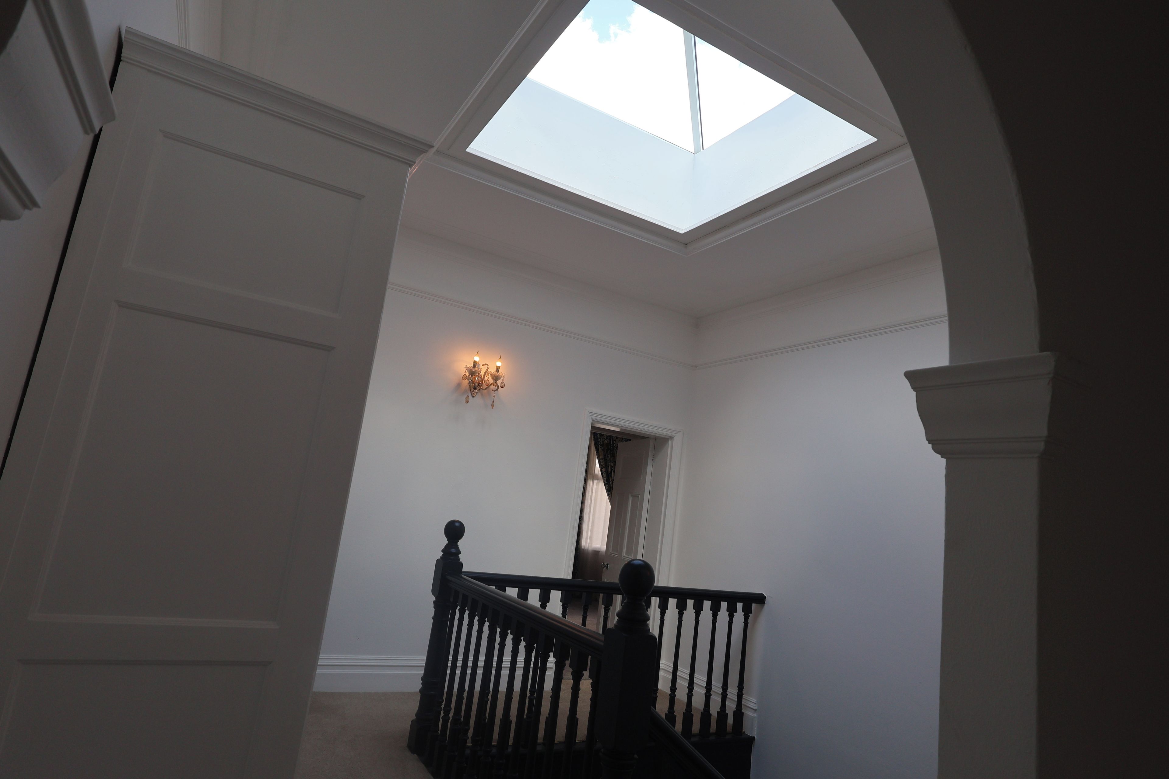 A staircase with a skylight leading to a second floor, a wall-mounted light fixture, and a door at the top of the stairs.