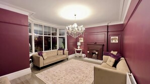 Una sala de estar con un sofá color beige, una chimenea, un candelabro y un ventanal grande.