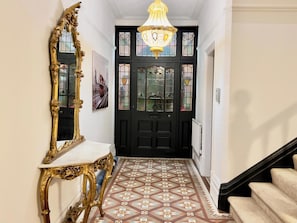 A hallway with a black door, a gold-framed mirror, a chandelier, and a patterned floor. - House-sleeps10-hottub-garden-parking-10mintotown (Burton on Trent)