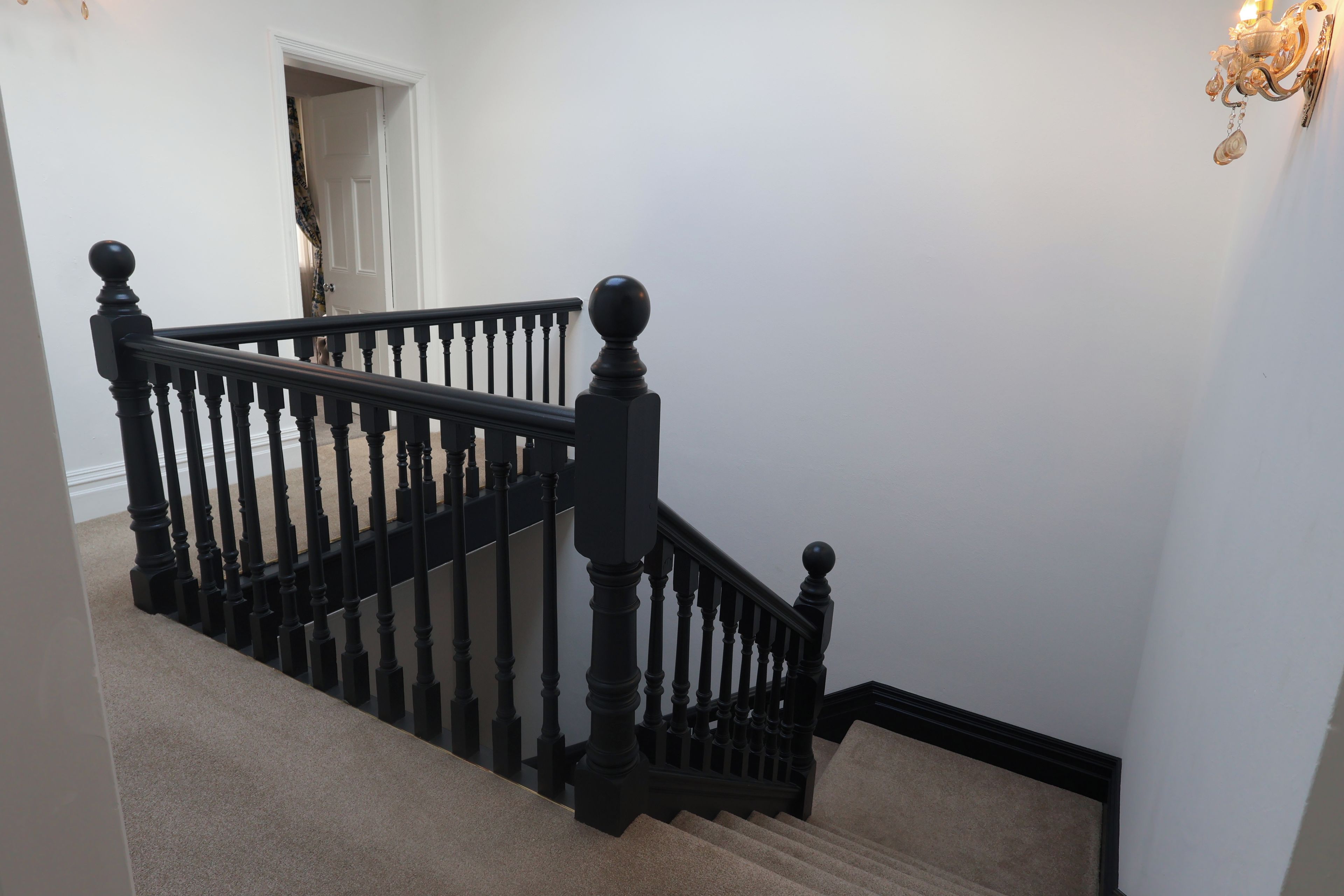 A staircase with black balusters and a handrail, carpeted steps, and a white door at the top.