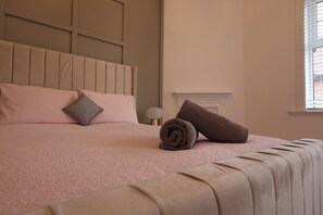 Una cama bien tendida con una colcha rosa, un cabecero y dos almohadas.
