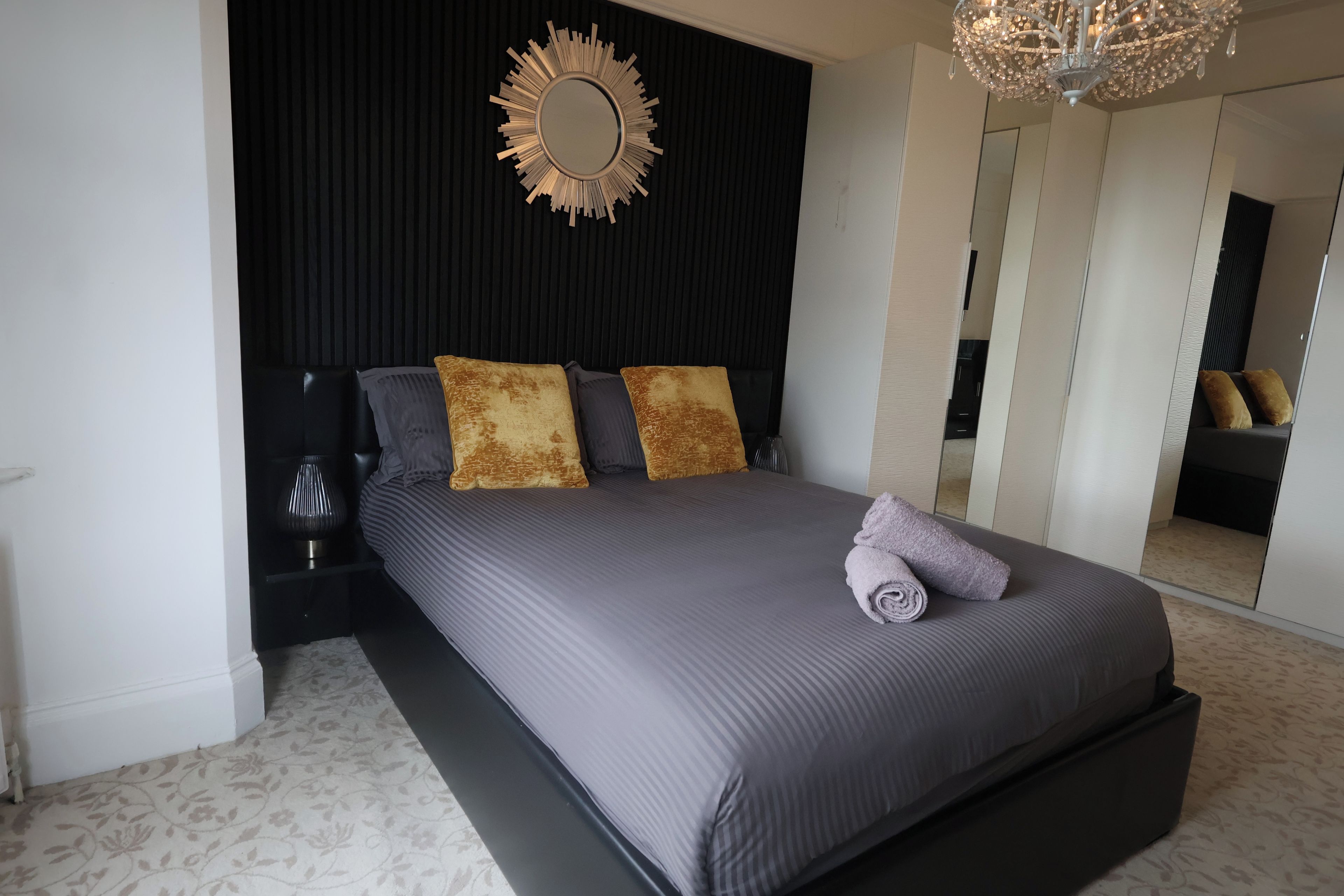 A modern bedroom with a large bed, a mirror, and a chandelier.