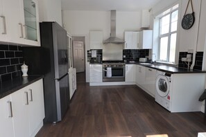 A modern kitchen with a stainless steel refrigerator, a built-in oven, and a washing machine. - The Shobnall House - Newly Refurbished, 5 Bedrooms (Burton on Trent)
