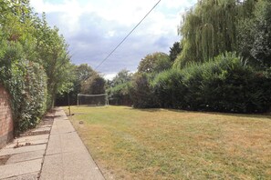 A grassy outdoor area with a soccer goal, surrounded by dense foliage and a brick wall on one side. - The Shobnall House - Newly Refurbished, 5 Bedrooms (Burton on Trent)