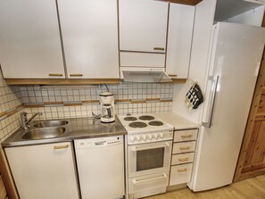 A compact kitchen with white cabinets, a built-in stove, a dishwasher, and a refrigerator. - Puolukka 2 by Interhome (Loviisa)