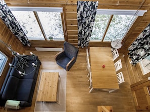A cozy cabin interior with a wooden floor, a sofa, a chair, a table, and curtains.