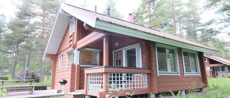 A two-story cabin with a porch, large windows, and a chimney.