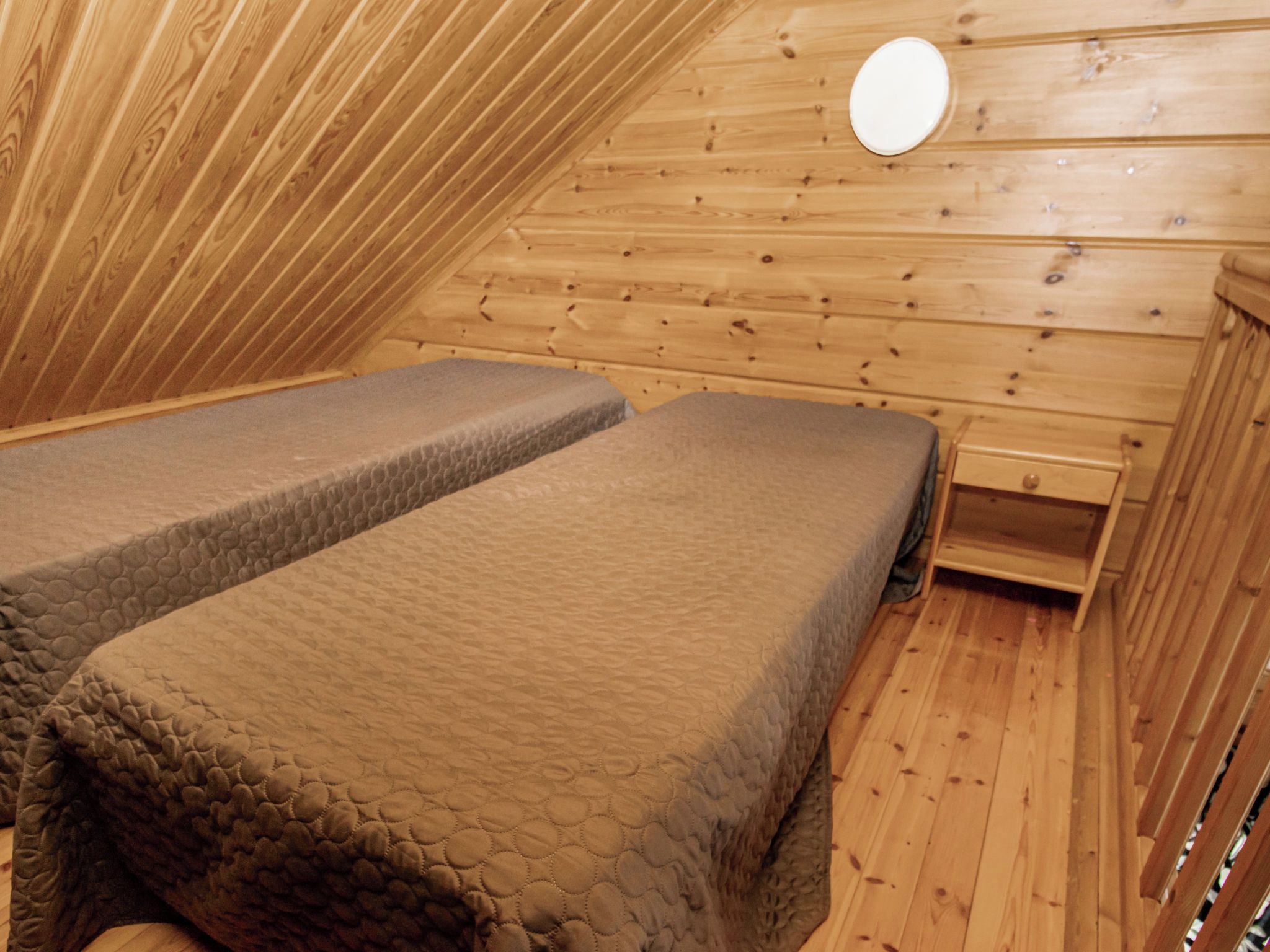 Una habitación pequeña y acogedora con dos camas, paredes de madera y un banco sencillo de madera.