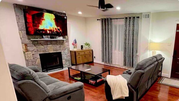 Uma sala de estar com lareira de pedra, televisão de tela plana, sofá e mesa de centro.