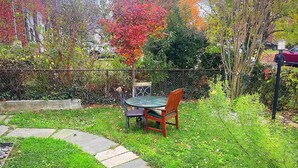 Um jardim com mesa e cadeiras, um caminho de pedra e uma cerca.