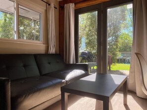A room with a leather sofa, a small table, and a sliding glass door leading to an outdoor area with a grill. - South Shore Suites (Bayfield)