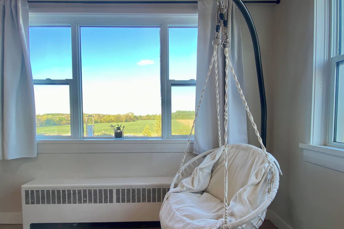 A room with a hanging chair by a window with a view of a green field.