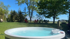 A hot tub in a backyard with a grassy lawn, trees, and red chairs. - South Shore Suites (Bayfield)