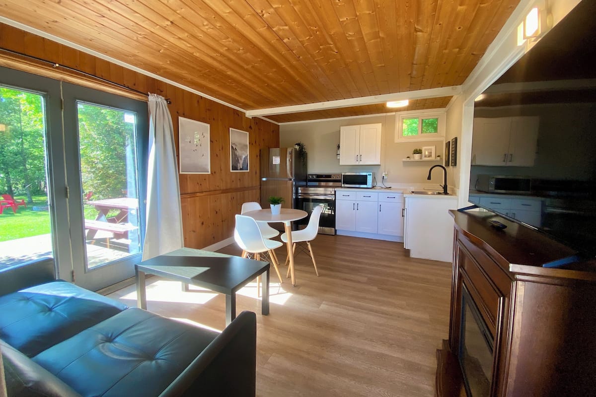 A modern cabin interior with a dining area, kitchen, and a seating area with a view of the outdoors.