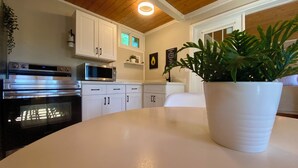 A modern kitchen with white cabinetry, a built-in oven, a microwave, and a potted plant on the counter. - South Shore Suites (Bayfield)