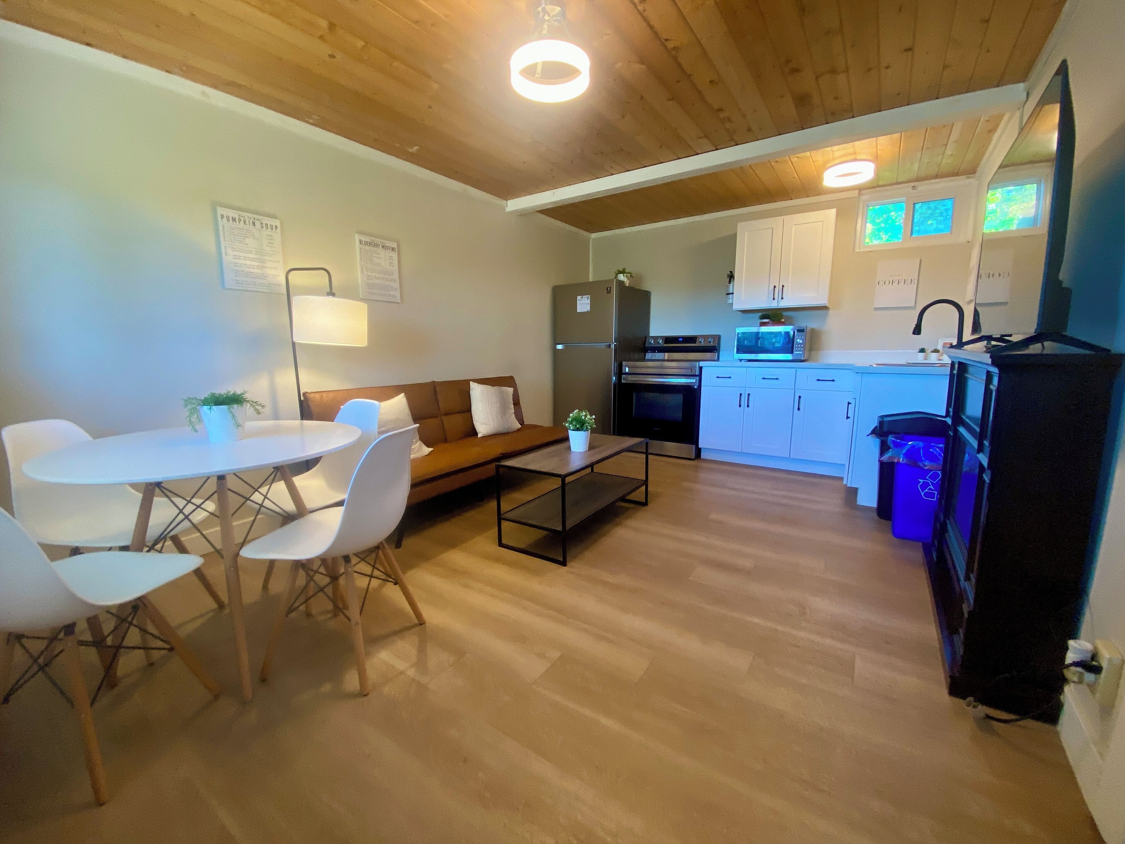 A compact kitchen with a refrigerator, oven, microwave, and sink. There is a dining area with a table and chairs, and a sofa.