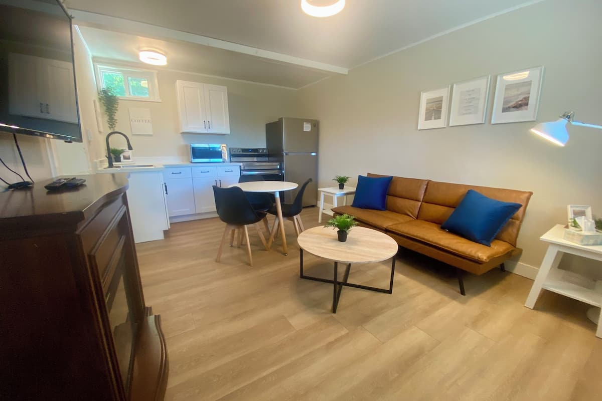 A modern living room with a brown leather sofa, a round coffee table, and a dining area with a white table and chairs.
