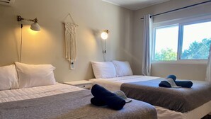 A hotel room with two beds, a bedside table, a wall-mounted lamp, and a window with curtains. - South Shore Suites (Bayfield)