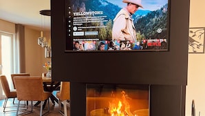 Un soggiorno moderno con una TV a schermo piatto sopra un caminetto, un'area pranzo con sedie e un tavolino da caffè in legno.