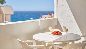 Ein runder, weißer Tisch mit zwei Stühlen, einer Erdbeerschale und zwei Gläsern Weißwein auf einem Balkon mit Meerblick.