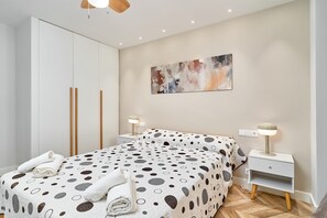 Een slaapkamer met een bed, nachtkastje, lamp, schilderij en een kledingkast.