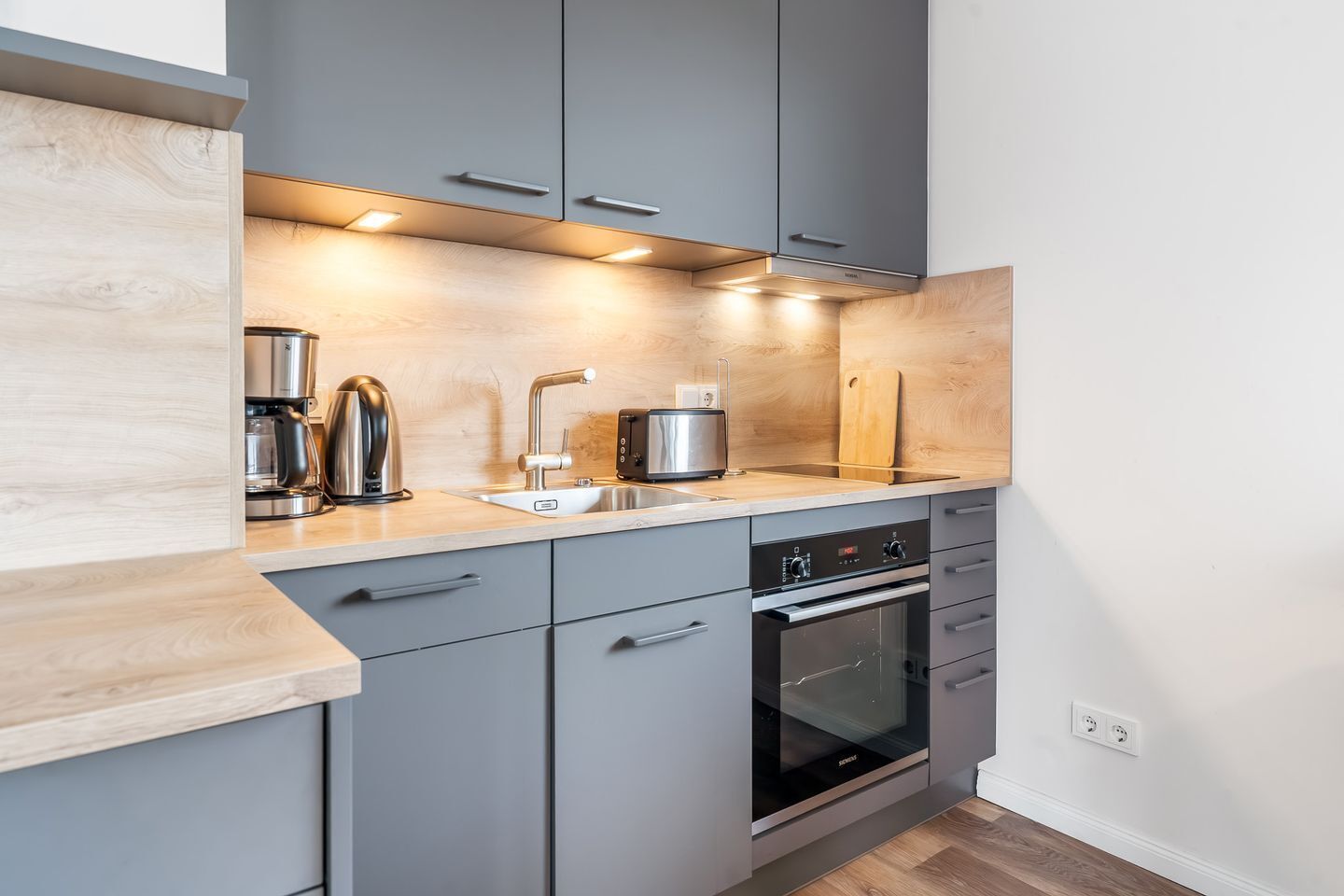 Een moderne keuken met grijze kastjes, een inbouwoven en een koffiezetapparaat.