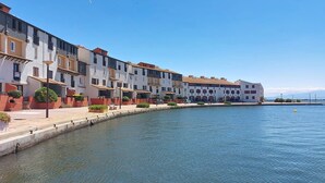 Ein Gebäude an der Uferpromenade mit Balkonen und einem gepflasterten Weg, vor dem sich ruhiges Wasser erstreckt.