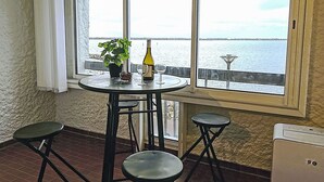 Ein kleiner Balkon mit Tisch, zwei Hocker, einem Blumentopf, einer Weinflasche und einem Glas.