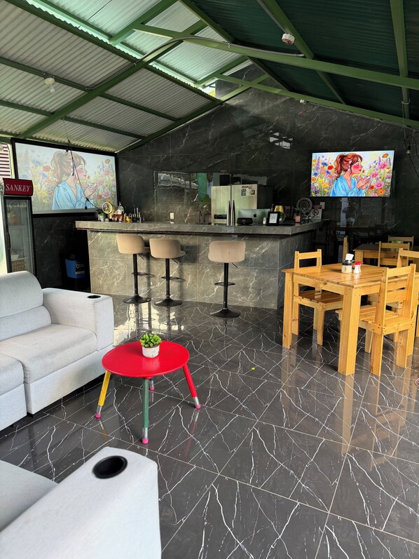 Un interior moderno con un sofá, una mesa roja con una planta, una zona de bar con taburetes y un televisor mostrando una escena floral.