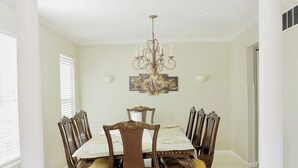 Een eetkamer met een kroonluchter, een tafel gedekt voor vier personen en een groot raam met jaloezieën.