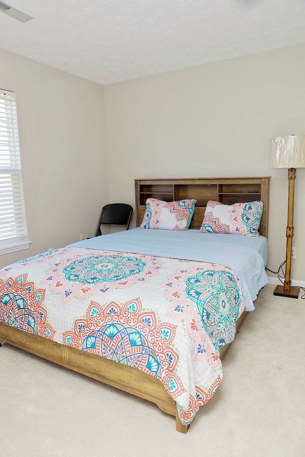 Quarto com estrutura de cama de madeira, colcha estampada e abajur.