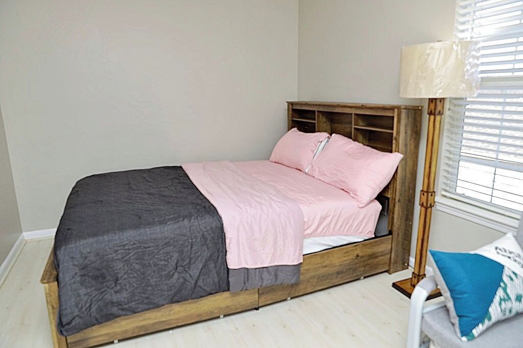 Un letto singolo con struttura in legno, copripiumino grigio e rosa, e una lampada da comodino.