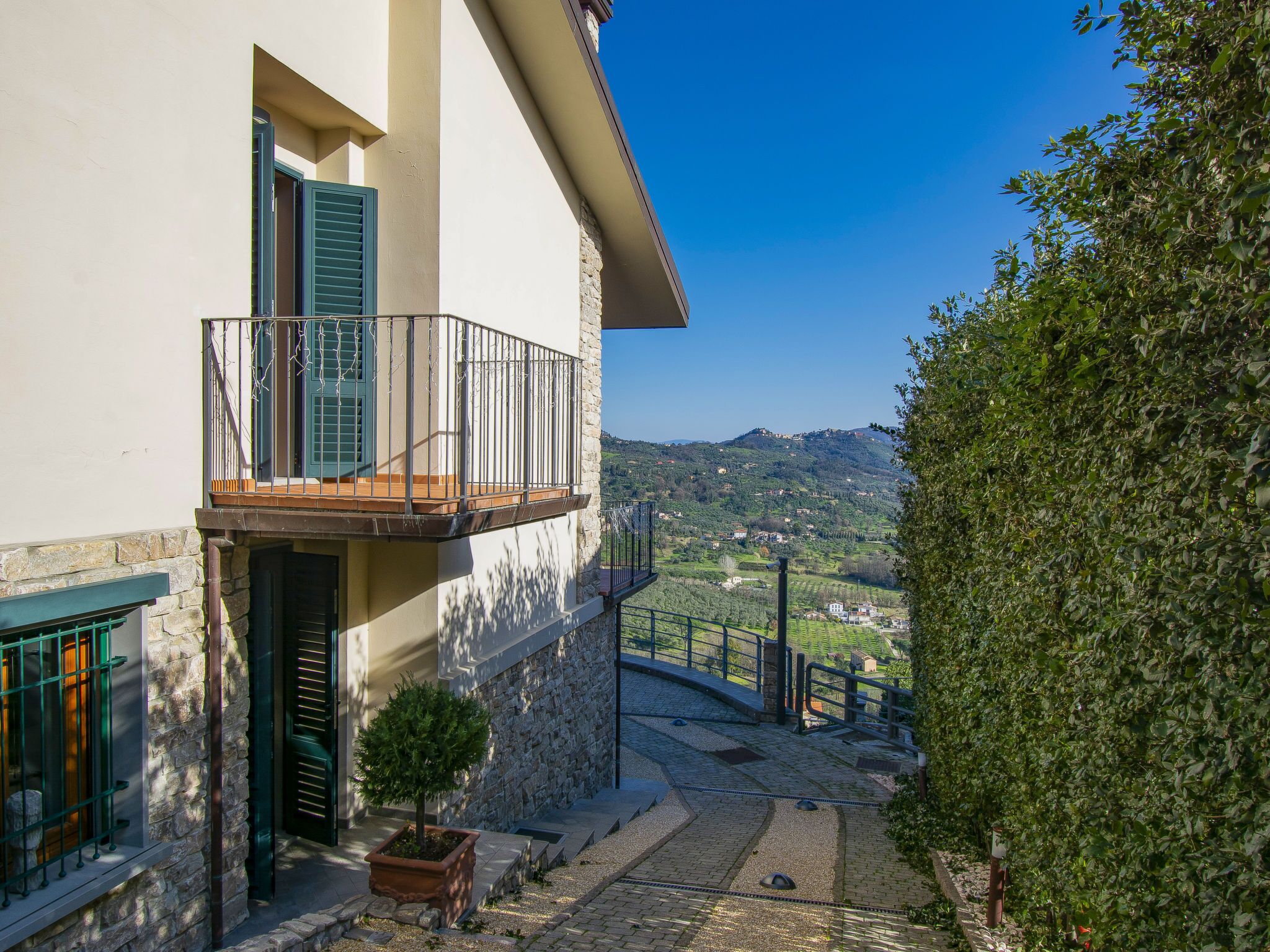 A two-story building with a balcony, stone walls, and a view of a hilly landscape.