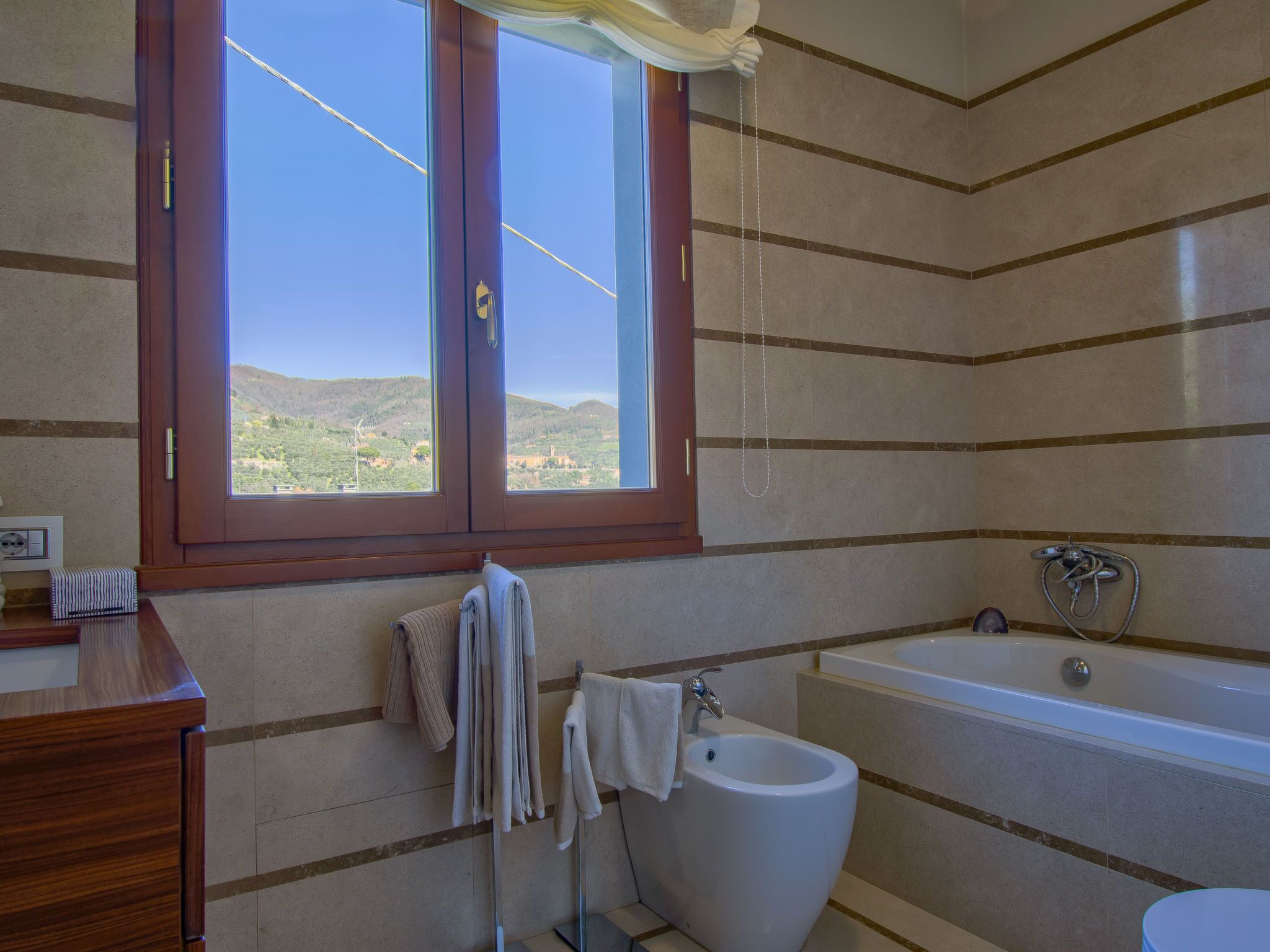 A bathroom with a bathtub, a bidet, and a window with a view of hills.