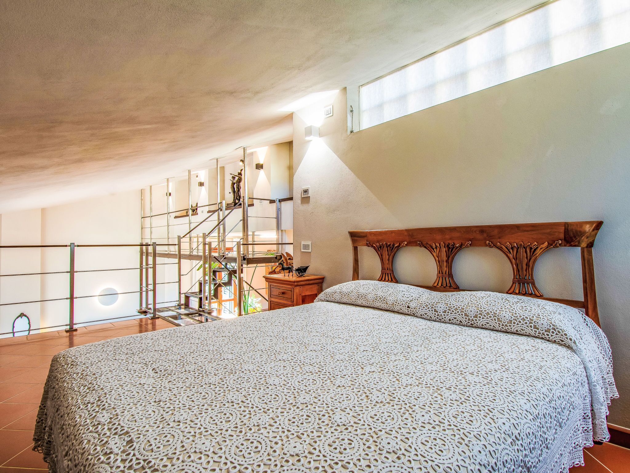 A bedroom with a large bed, a wooden headboard, a nightstand, and a window with natural light.