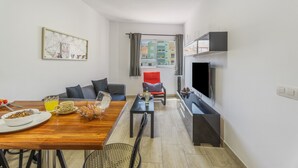 A modern apartment with a dining area, a living room with a sofa and a red chair, a TV mounted on the wall, and a window with curtains. - Vacation 'Ifae 3' with Wi-Fi (Guía de Isora)