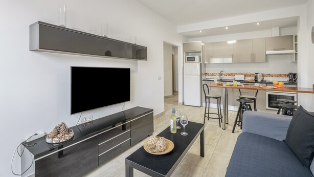 A modern living room with a flat-screen TV, a dark wooden coffee table, a sofa, and a kitchen area with a bar and stools. - Vacation 'Ifae 3' with Wi-Fi (Guía de Isora)