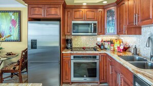 A kitchen with wooden cabinets, a stainless steel refrigerator, a microwave, an oven, and a sink. - Sugar Beach #131: Front-row views, salty air & instant beach access—pure Maui! (Kihei, Maui)