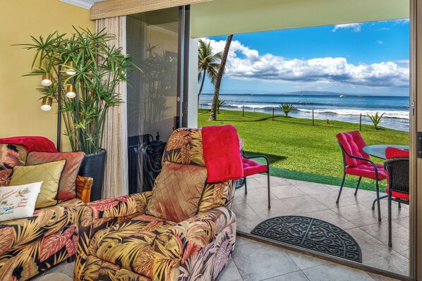 Ein Zimmer mit einem tropisch gestalteten Sofa, einem roten Sessel und Blick auf das Meer.