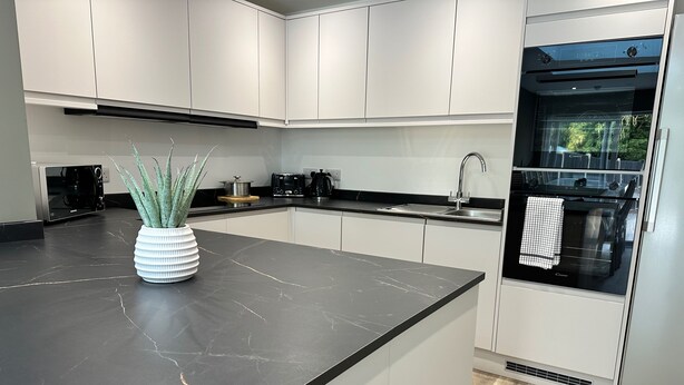 Eine moderne Küche mit weißen Schränken, einer schwarzen Marmorarbeitsplatte und einem eingebauten Backofen.