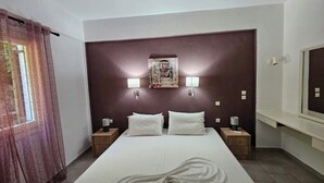 A hotel room with a large bed, two bedside tables, a nightstand, a mirror, and a wall-mounted artwork.