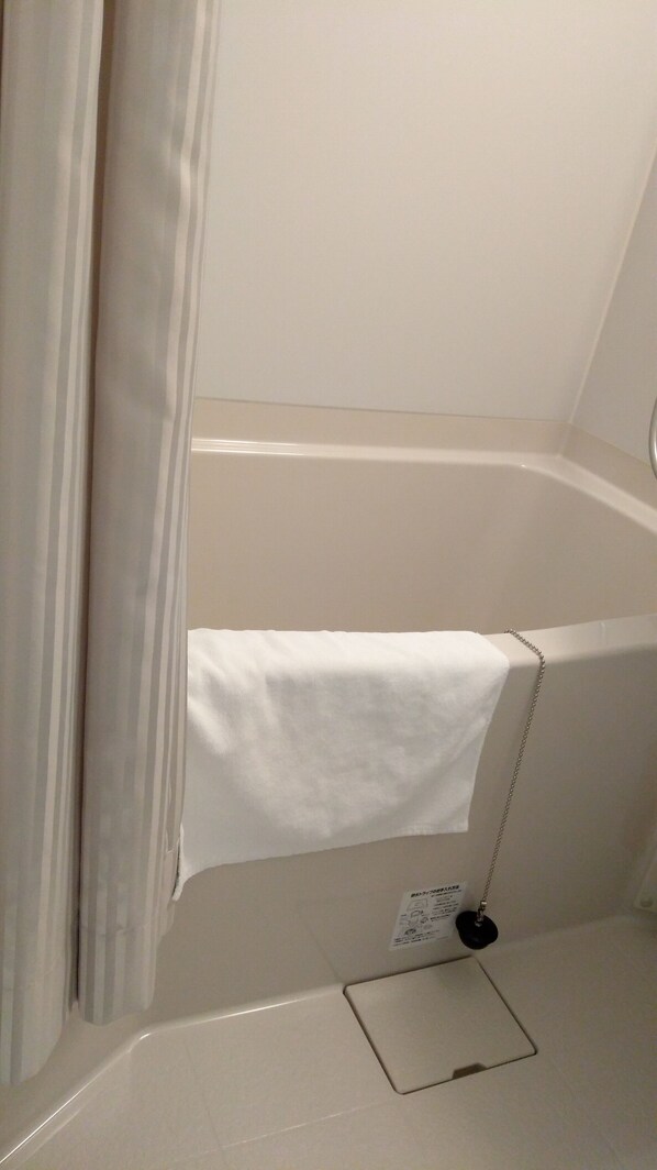 A bathroom with a bathtub, a towel hanging on the side, and a small shelf with a power outlet.