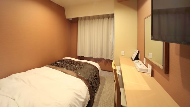 Una habitación de hotel con cama, escritorio, teléfono y televisor.