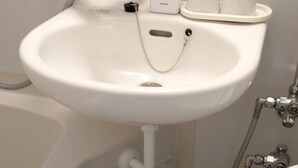 Un lavamanos con grifo, dispensador de jabón y tres tazas. Debajo del lavamanos, hay un estante con tres botellas de jabón líquido.