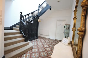 Un escalier avec un sol à motifs, une porte blanche et un miroir encadré de doré.