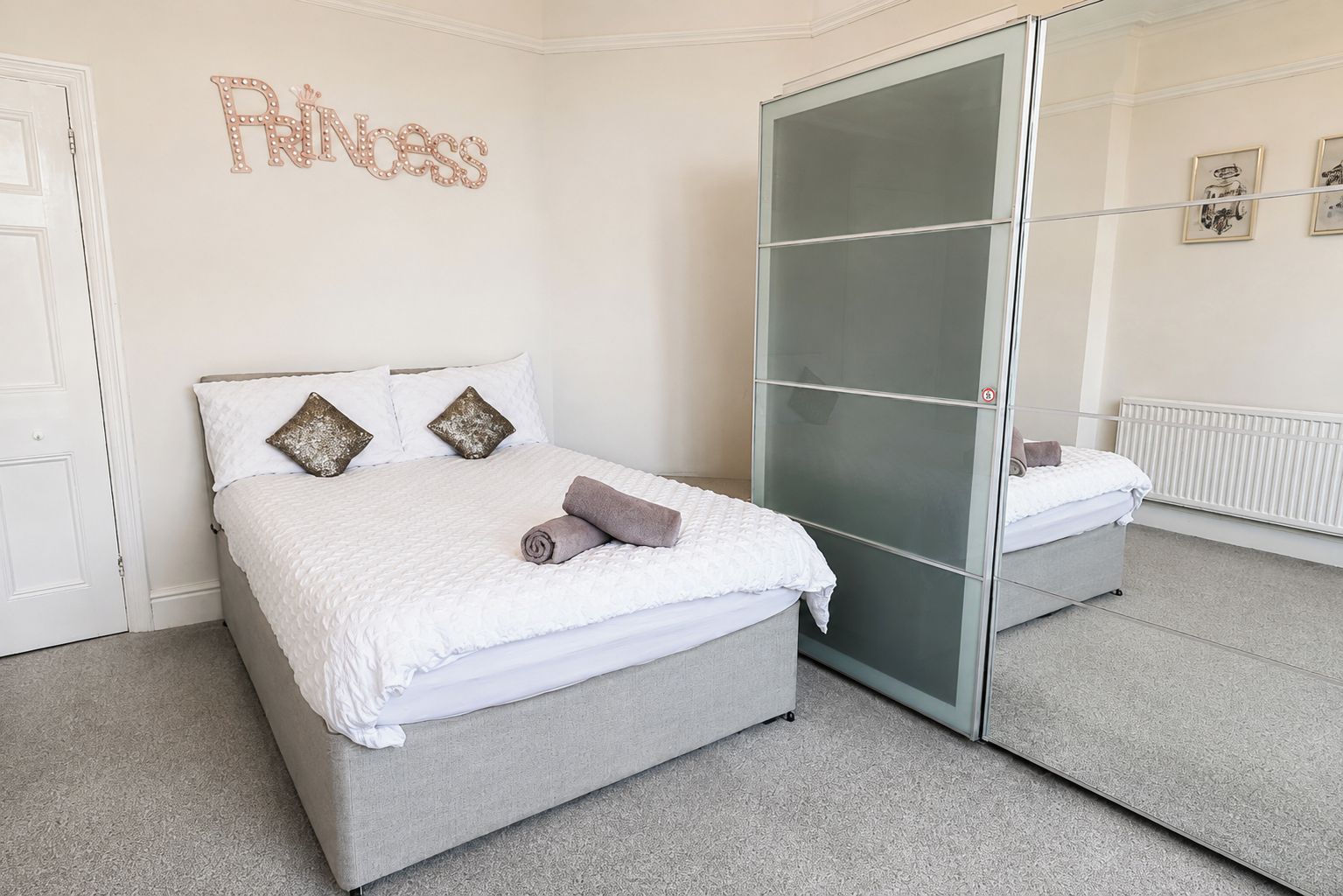 A bedroom with a bed, a wardrobe, a mirror, and a wall decoration.
